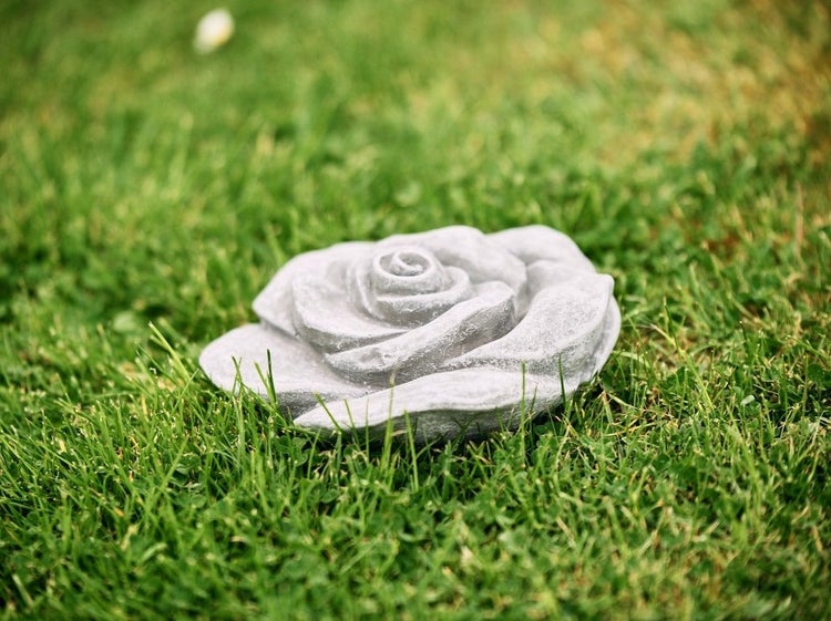 Dekorative Rosenblüte aus Stein als Gartenfigur für den Außenbereich im Gras liegend