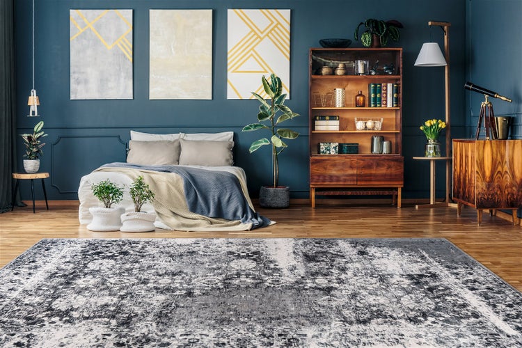 Modernes Schlafzimmer mit grau gemustertem Teppich, dunkelblauer Wand mit Kunst, Holzregal, Bett mit Textilien und Zimmerpflanzen.