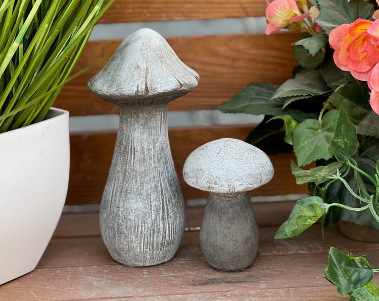 Zwei Deko-Pilze aus Stein für den Garten, ein hoher und ein kleiner Pilz, platziert neben Pflanzen.