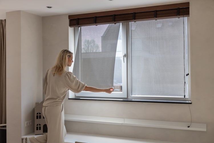 Frau bedient ein Fensterrollo im Wohnzimmer