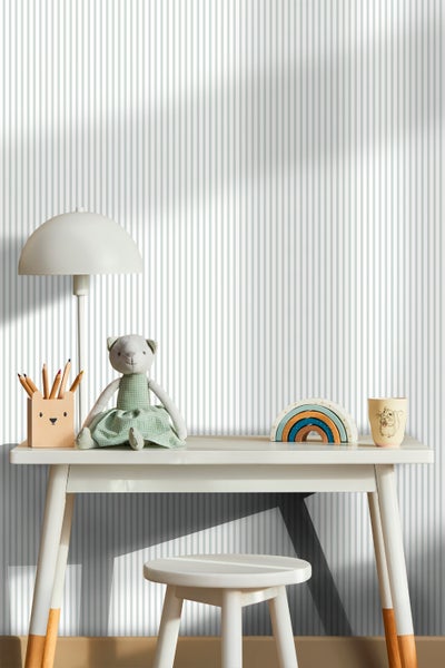 Kinderschreibtisch mit Stuhl, Lampe, Spielzeug und Stiften vor einer gestreiften Tapete
