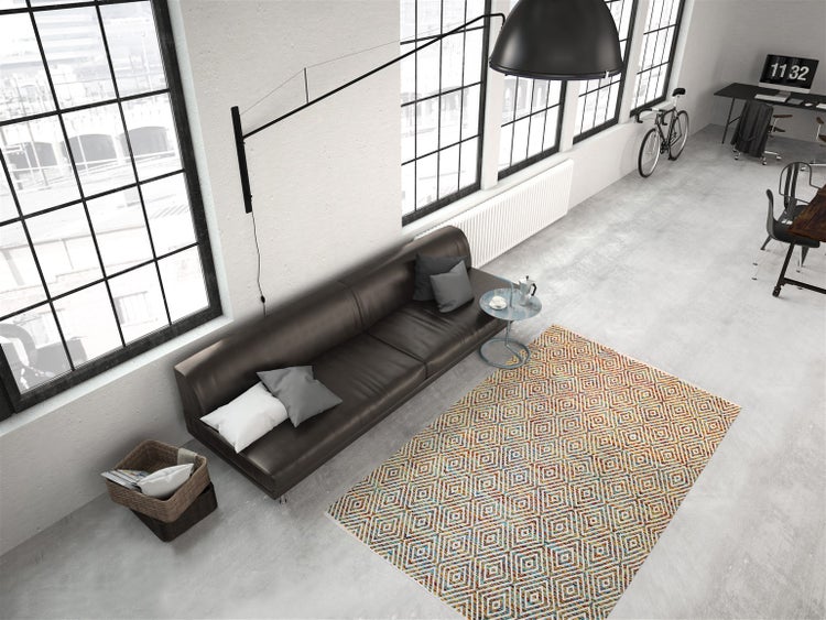 Industrielles Loft mit einem bunt gemusterten Teppich mit Rautenmuster auf grauem Betonboden, einem dunklen Ledersofa und großen Fenstern.