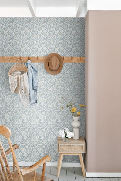 Hell gestalteter Innenraum mit floral gemusterter Tapete, einer Holzgarderobe, einem Beistelltisch und einem rustikalen Holzstuhl.