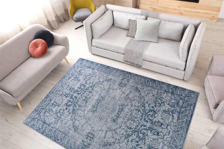 Vintage-Teppich mit blau-grauem Medaillon-Muster in einem hellen Wohnzimmer mit grauen Sofas und Holzboden.