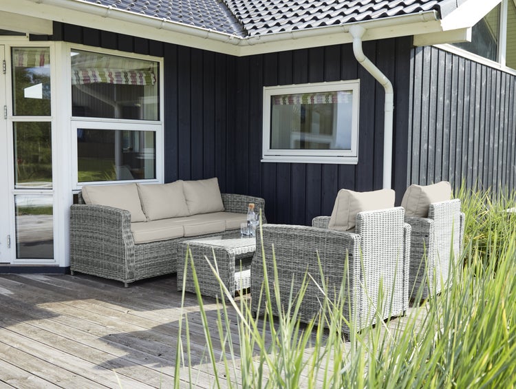 Gartenmöbelset aus Rattan mit Sofa, Sesseln und Tisch auf einer Terrasse vor einem Haus.