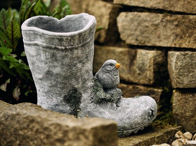 Gartendekoration aus Stein in Form eines Stiefels als Pflanzgefäß mit einem kleinen Vogel als Verzierung.