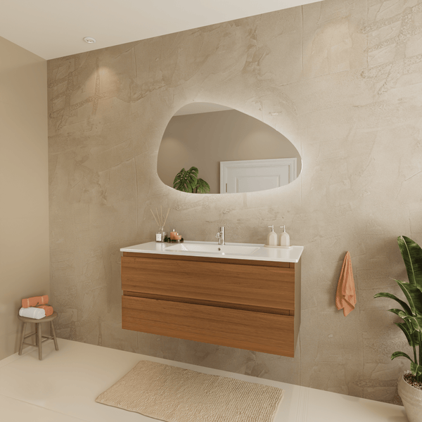 Modernes Badezimmer mit Waschtischunterschrank aus Holz, weißem Waschbecken und organisch geformtem LED Spiegel vor einer strukturierten Wand.