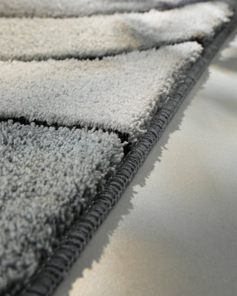 Detailaufnahme eines Hochflor-Teppichs mit Wellenmuster und gekettelter Kante.