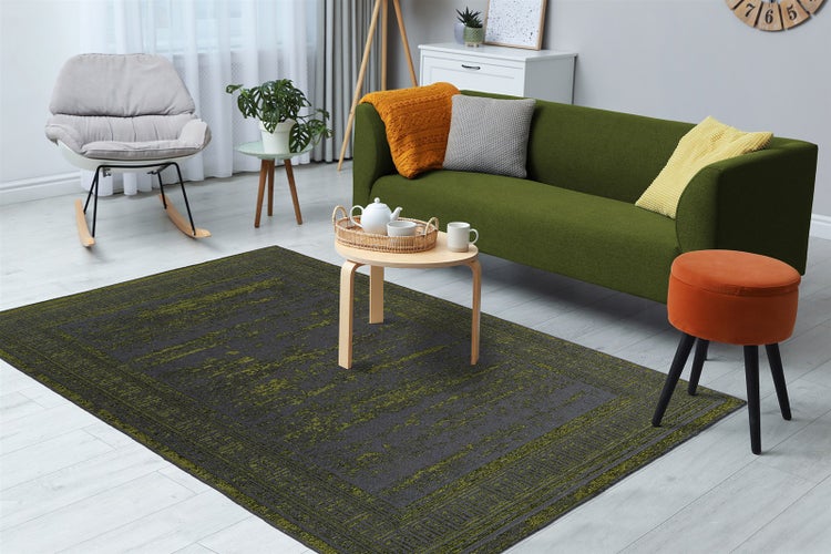 Dunkelgrauer Teppich mit hellgrünem Muster in einem modern eingerichteten, hellen Wohnzimmer mit grünem Sofa und grauem Schaukelstuhl.