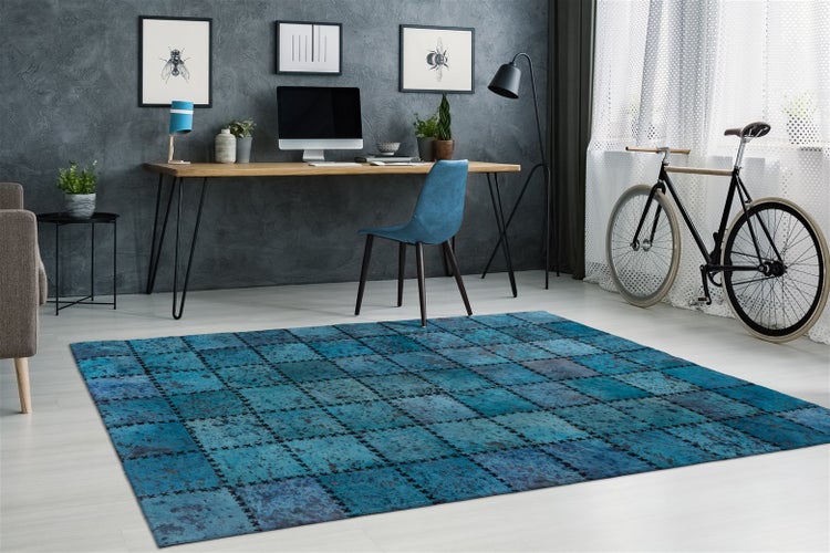 Moderner blauer Patchwork-Teppich in einem hellen Arbeitszimmer mit Holzschreibtisch, blauem Stuhl und Fahrrad am Fenster.
