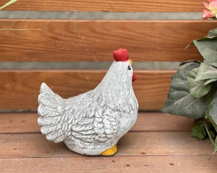 Dekorative Gartenfigur Huhn in Steinoptik mit rotem Kamm auf einer Holzterrasse.