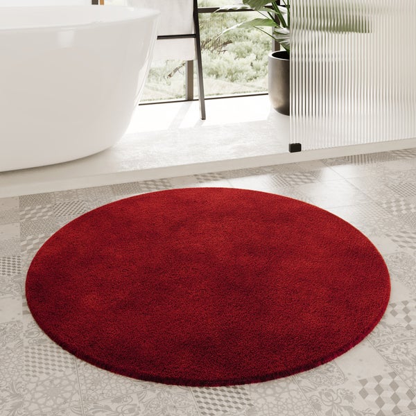 Runder, roter Badteppich auf gemusterten Bodenfliesen in einem hellen Badezimmer neben einer weißen Badewanne.