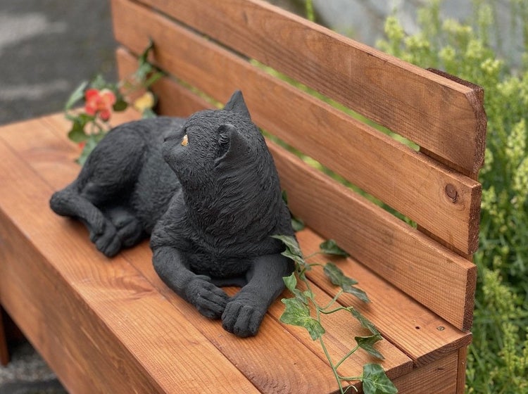 Dekorative Katzenfigur aus Kunststein, liegend auf einer hölzernen Gartenbank.