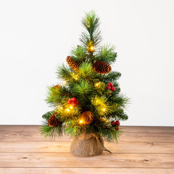 Dekorativer Weihnachtsbaum mit Beleuchtung, Zapfen und Beeren auf einem Holztisch