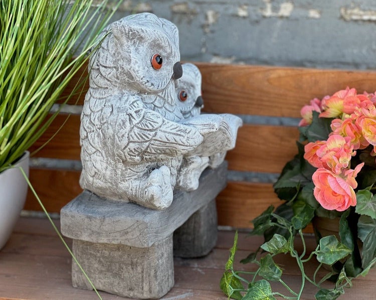 Gartenfigur aus grauem Stein: Zwei detaillierte Eulen sitzen auf einer Bank und lesen gemeinsam in einem Buch.