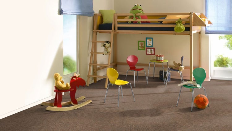 Hell eingerichtetes Kinderzimmer mit braunem Teppichboden, einem Hochbett aus Holz, bunten Kinderstühlen und einem Schaukelpferd.