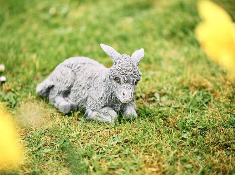 Dekorative Gartenfigur in Form eines liegenden Esels aus wetterfestem Material im Gras platziert
