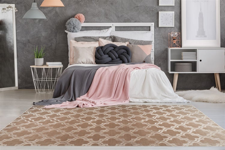 Modernes, helles Schlafzimmer mit weißem Bett, dekorativen Kissen und einem beigefarbenen Teppich mit geometrischem Muster.