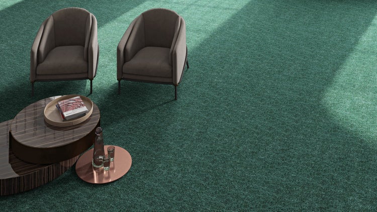 Helles Zimmer mit grünem, strukturiertem Teppichboden, zwei modernen Sesseln und einem Couchtisch aus Holz.