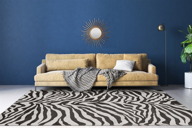 Moderner Wohnraum mit einem Teppich im Zebralook, einem beigen Sofa mit Kissen und Decke, einem Sonnenspiegel, einer Stehlampe und einer Zimmerpflanze.