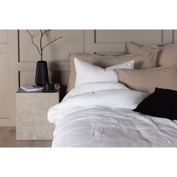 Modernes Schlafzimmer mit weißer Bettwäsche aus Leinen, beigen und schwarzen Kissen, Marmor-Nachttisch und Wandpaneelen.