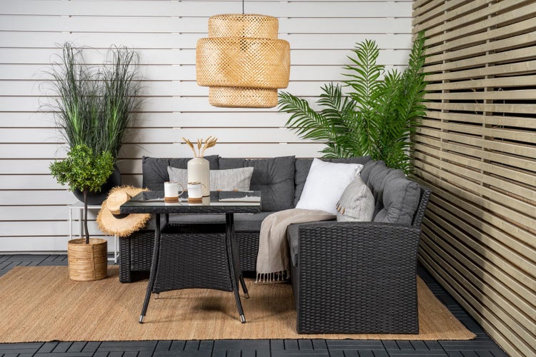Terrassenszene mit Rattan-Lounge-Set, Tisch mit Glasplatte, Hängelampe und dekorativen Pflanzen
