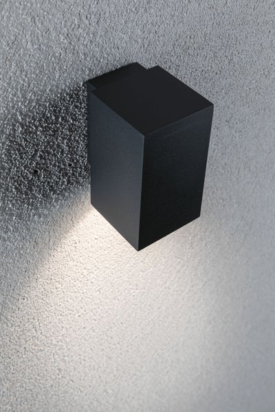 Moderne quaderförmige Außenwandleuchte mit Lichtkegel an einer strukturierten Fassade.