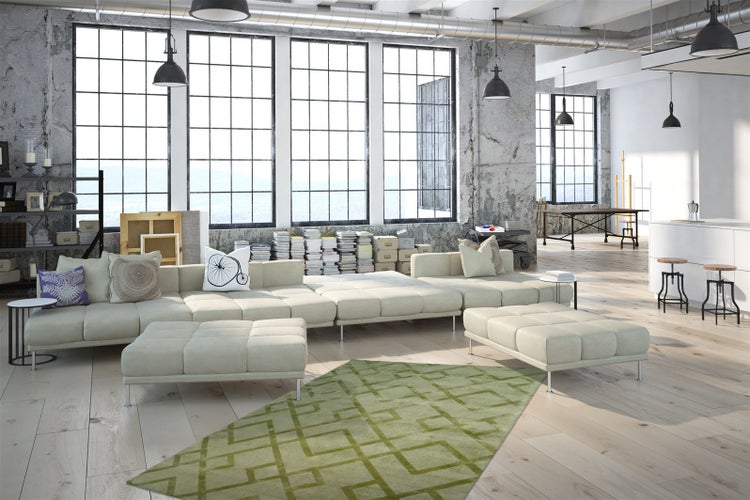 Geräumiges Loft im Industriedesign mit großem Modulsofa, grünem Teppich mit geometrischem Muster, Holzboden und großen Fenstern an Betonwänden.
