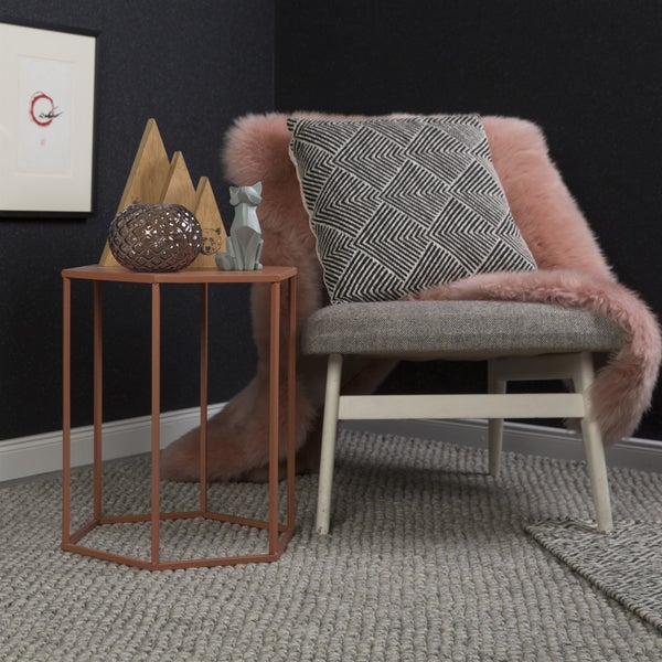 Moderner Wohnbereich mit grauem Sessel, rosa Kunstfell, Kissen mit geometrischem Muster und sechseckigem Beistelltisch auf Teppich.