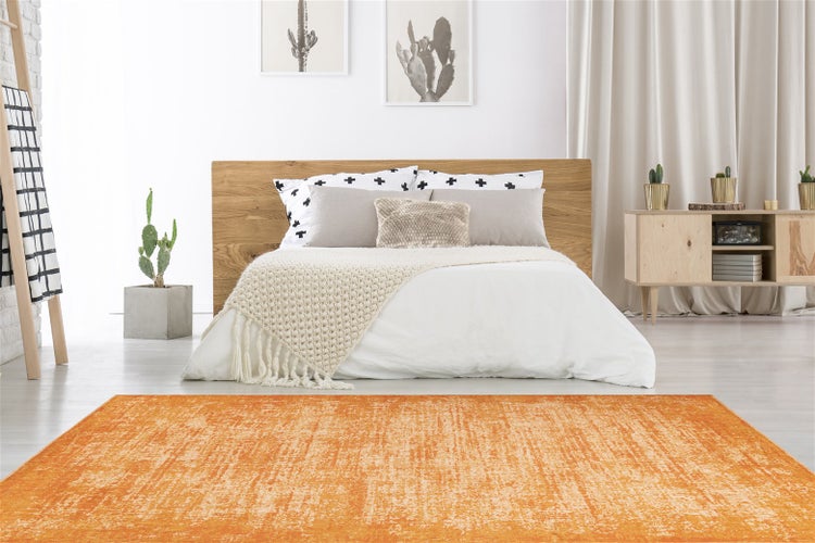 Rechteckiger orangefarbener Teppich mit Used-Look in einem hellen Schlafzimmer mit Holzbett, weißem Bettzeug und minimalistischer Dekoration.