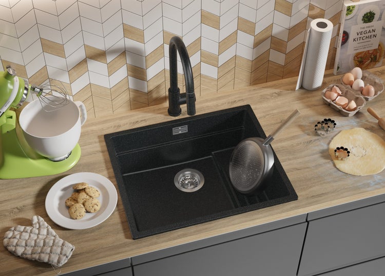 Küchenszene mit Spüle, Armatur, Küchenmaschine, Kochbuch, Eiern und Backutensilien auf einer Arbeitsplatte.