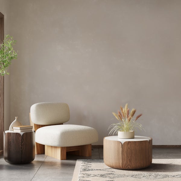 Modernes Wohnzimmer mit strukturierter Wandfarbe in Beige, gepolstertem Sessel, Holztischen und grauen Bodenfliesen.
