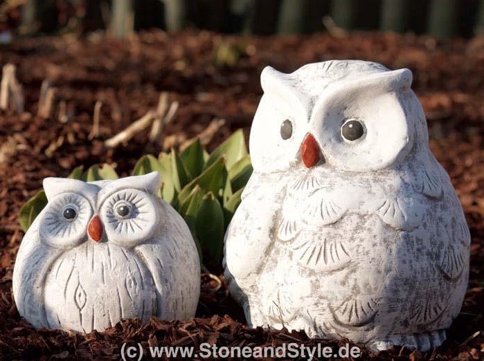 Zwei Eulenfiguren aus Steinguss für die Gartendekoration stehen auf Rindenmulch.