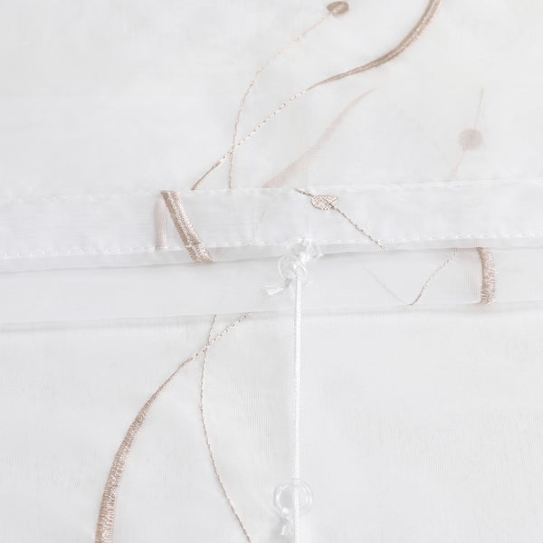 Detailansicht eines weißen, transparenten Rollos mit Stickerei und Zugschnur