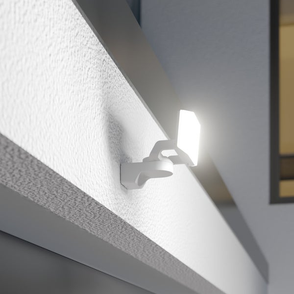 Moderner weißer LED-Außenstrahler an einer weißen strukturierten Wand unter einem Dachvorsprung montiert, strahlt helles Licht aus.