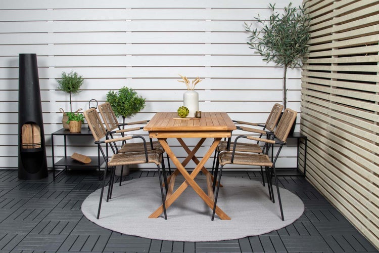 Gartenszene mit Holztisch, Stühlen mit Flechtsitz, Pflanzen und Kaminofen auf einer Terrasse