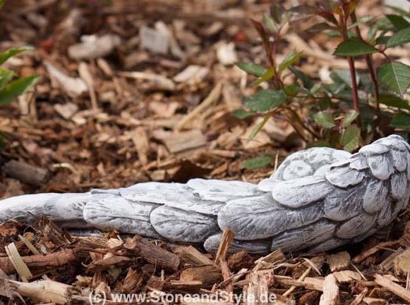 Steinfigur in Form eines Engelsflügels als Gartendeko auf Rindenmulch