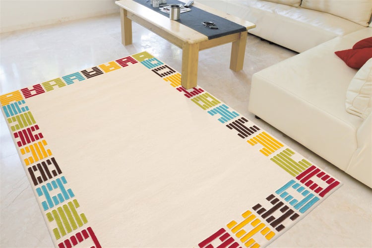 Heller Teppich mit buntem geometrischem Muster am Rand im Wohnzimmer mit weißem Sofa und Couchtisch aus Holz auf hellen Fliesen.