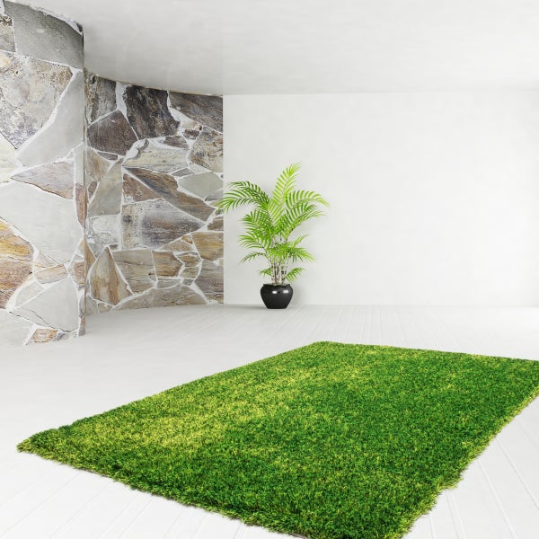 Rechteckiger grüner Hochflor-Teppich in einem hellen Raum mit Natursteinwand, weißem Boden und einer Zimmerpflanze.