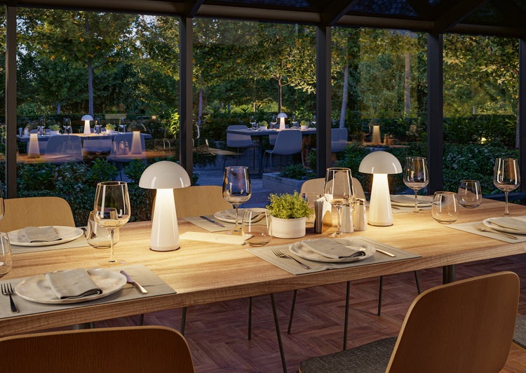 Gedeckter Esstisch mit zwei Tischleuchten in Pilzform in einem hellen Wintergarten mit Blick in den Garten am Abend.