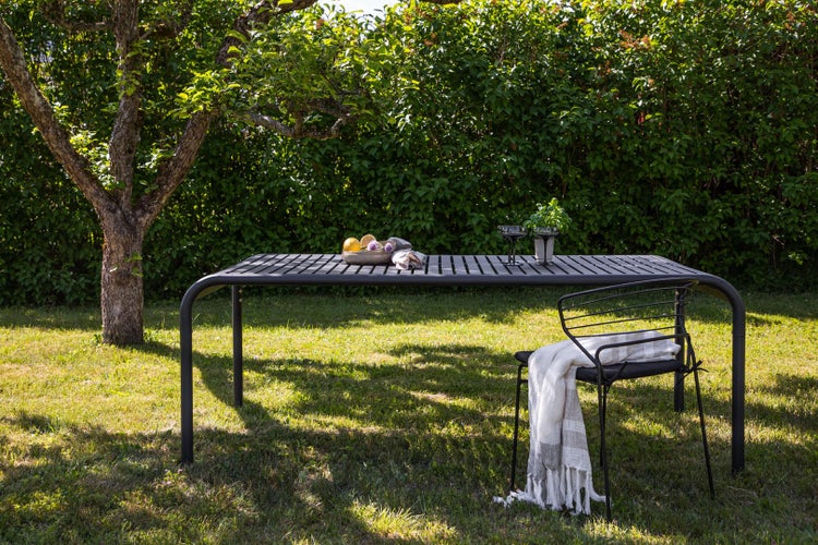 Gartenszene mit einem Gartentisch, einem Stuhl und Dekorationen im Freien auf einer Rasenfläche.