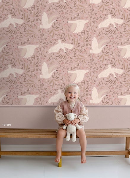 Kind sitzt vor einer Wand mit einer Tapete mit Schwanmotiv.