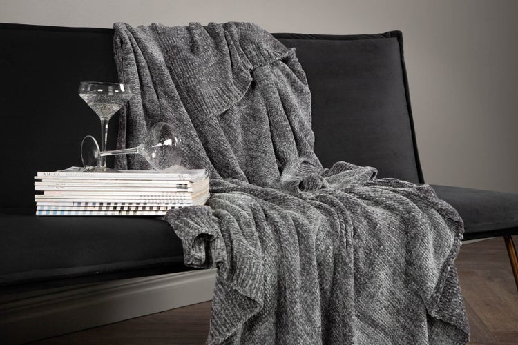 Graue Kuscheldecke auf einem Sessel drapiert, mit Zeitschriften und Gläsern