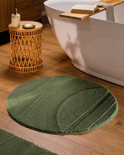 Runder Badezimmerteppich mit reliefartigem Wellenmuster vor einer Badewanne in einem Badezimmer mit Holzoptik Boden.