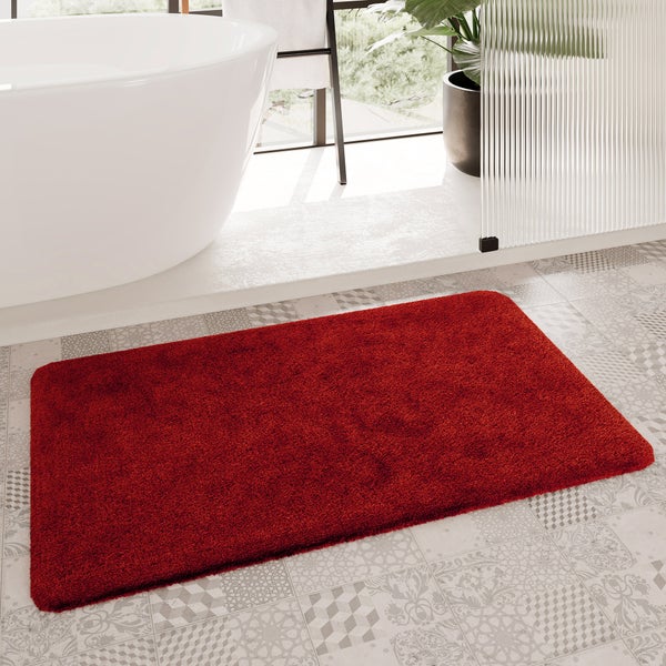 Roter Badteppich auf gemusterten Fliesen in einem hellen Badezimmer mit freistehender Badewanne und Glasabtrennung.