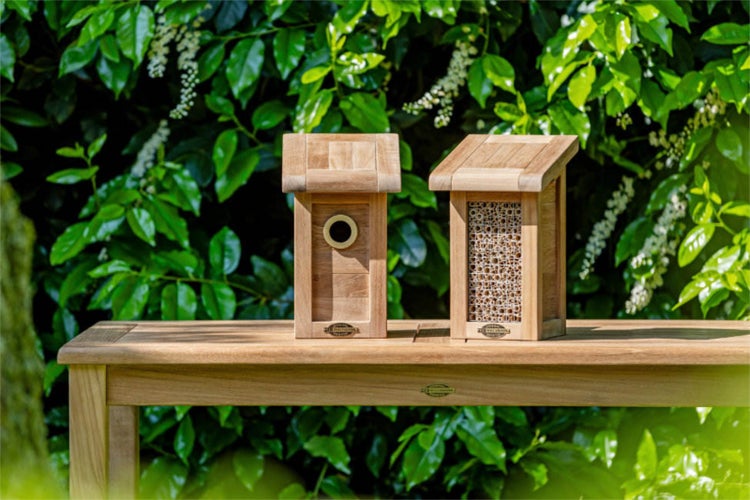 Zwei hölzerne Insektenhotels auf einem Gartentisch vor einem grünen Hintergrund.