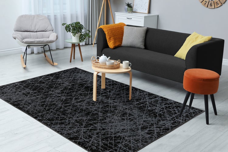 Großer dunkelgrauer Teppich mit abstraktem Muster in einem hellen, modernen Wohnzimmer mit Sofa, Couchtisch und Schaukelstuhl.