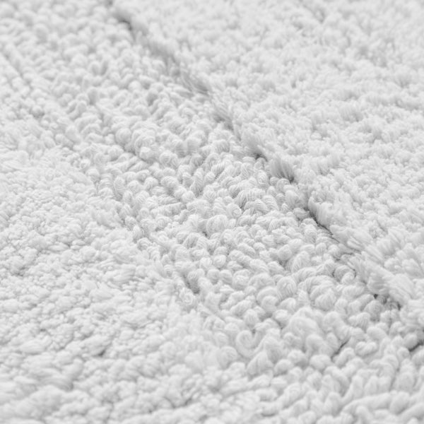 Nahaufnahme einer weißen flauschigen Badematte mit weicher Schlingenstruktur und dezentem Streifenmuster