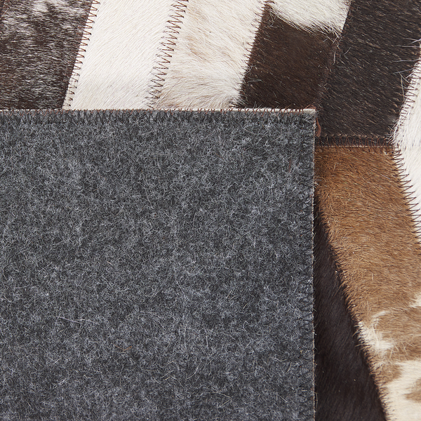 Detail eines Kuhfell-Patchwork-Teppichs mit sichtbarer Filzrückseite und dekorativen Nähten.