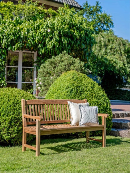 Holzgartenbank mit Kissen vor einer grünen Hecke